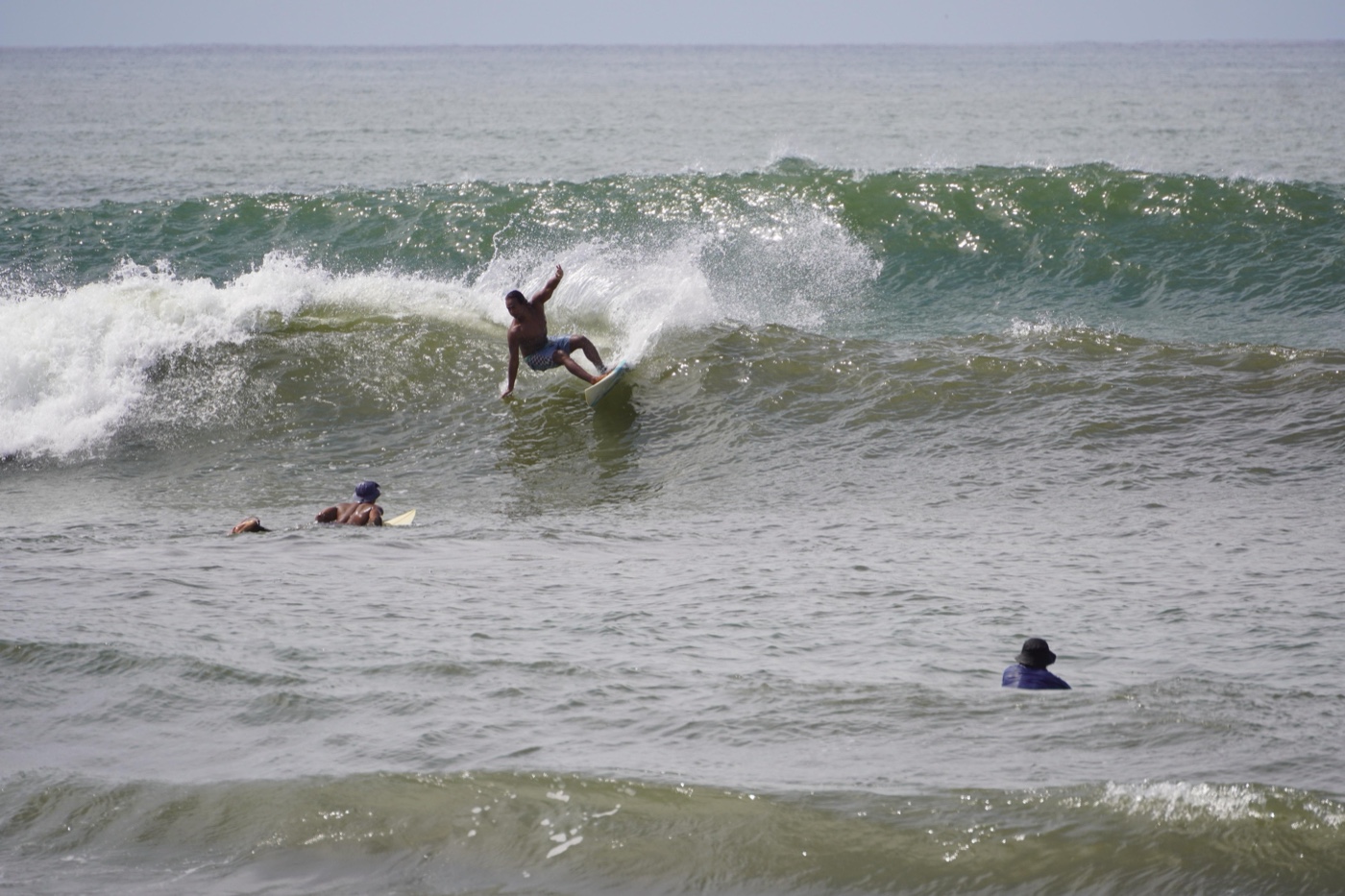 A surfer riding a green wave while others wait on their boards in the foreground.