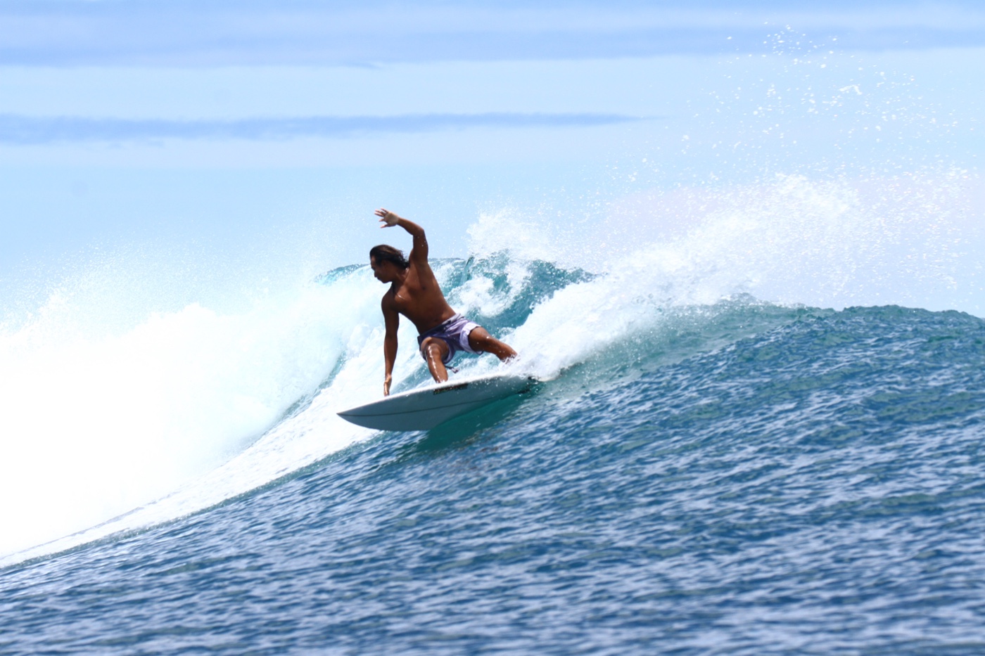 A surfer turning with one arm raised, throwing spray off the top of a wave.